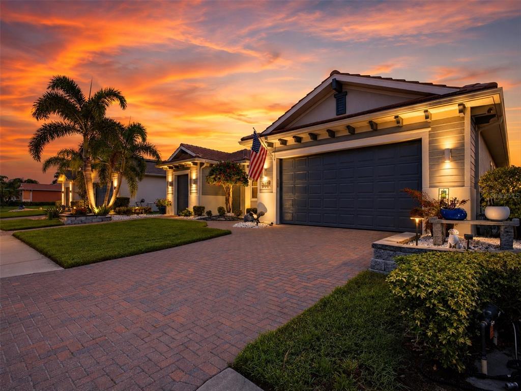 A single-story house with a brick paver driveway and an American flag at sunset — 5609 TIDEWATER PRESERVE BOULEVARD, BRADENTON, FL