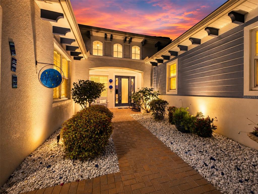 A brick walkway leads to the front entrance of a house with blue siding and landscaping — 5609 TIDEWATER PRESERVE BOULEVARD, BRADENTON, FL
