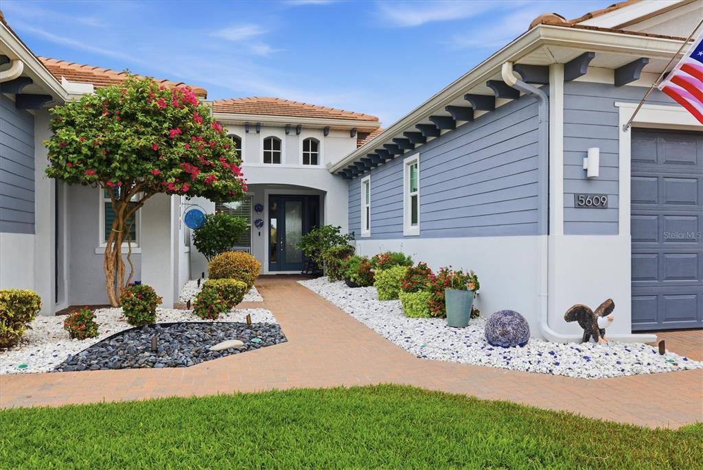 A blue house exterior features a paved walkway leading to the front entrance and landscaping — 5609 TIDEWATER PRESERVE BOULEVARD, BRADENTON, FL