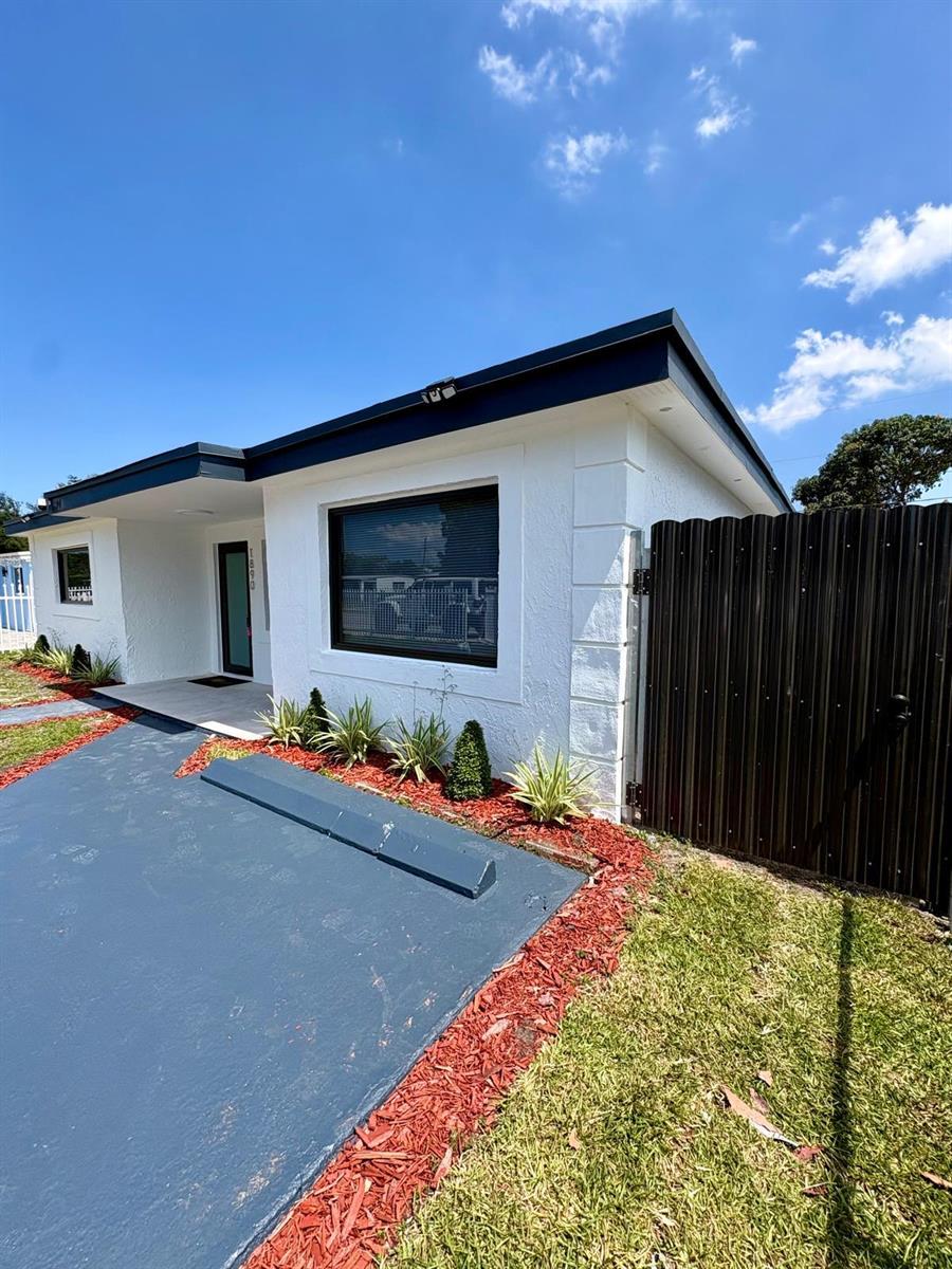 A white stucco building features a dark roof, a front door, and a metal fence — 1890 Rutland Street, Opa-Locka FL 33054, OPA-LOCKA, FL