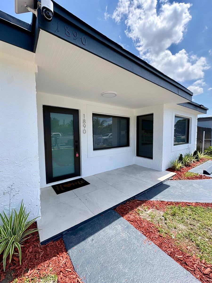 The exterior of a white house features a black front door, windows, and a porch — 1890 Rutland Street, Opa-Locka FL 33054, OPA-LOCKA, FL