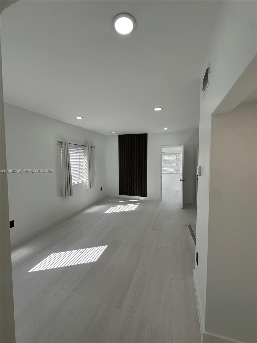 An empty room features light wood flooring, recessed lighting, and a dark vertical slat accent wall — 109 NW 6th Ave # 5, Miami FL 33128, MIAMI, FL