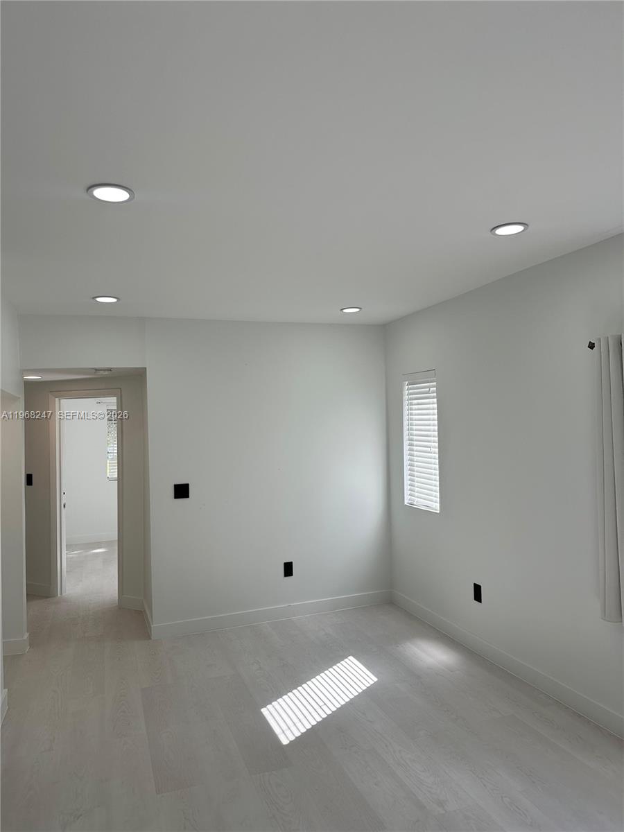 A minimalist room features white walls, light wood-look flooring, recessed lighting, and a doorway — 109 NW 6th Ave # 5, Miami FL 33128, MIAMI, FL
