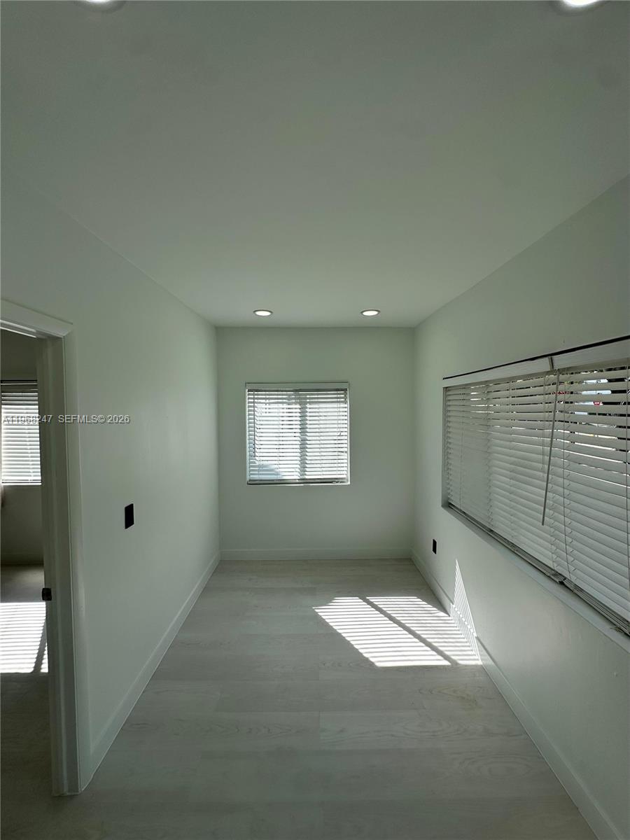 A narrow, empty room features light-colored wood-look flooring, white walls, and two windows with blinds — 109 NW 6th Ave # 5, Miami FL 33128, MIAMI, FL