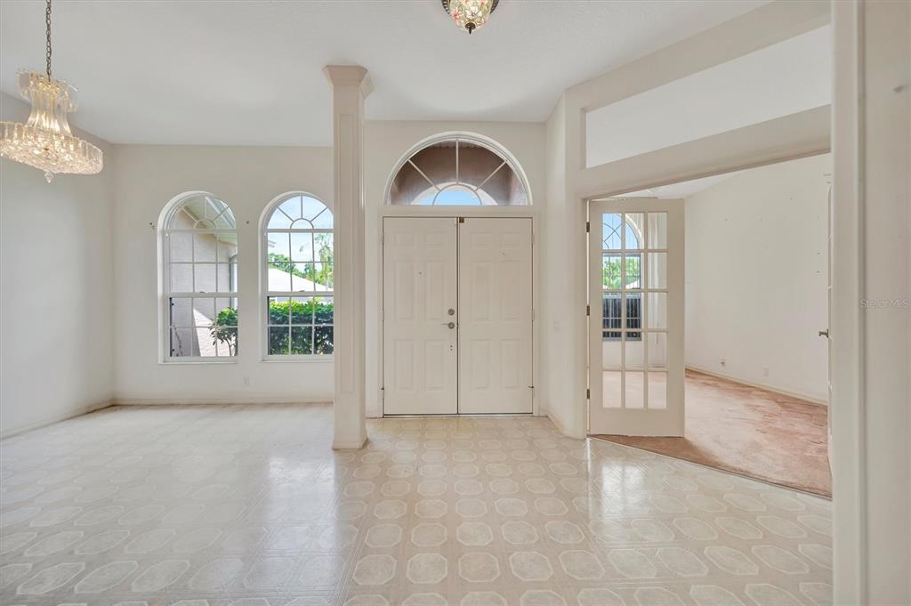A bright foyer features white double doors, arched windows, a column, and a chandelier — 4206 73RD TERRACE E, SARASOTA, FL