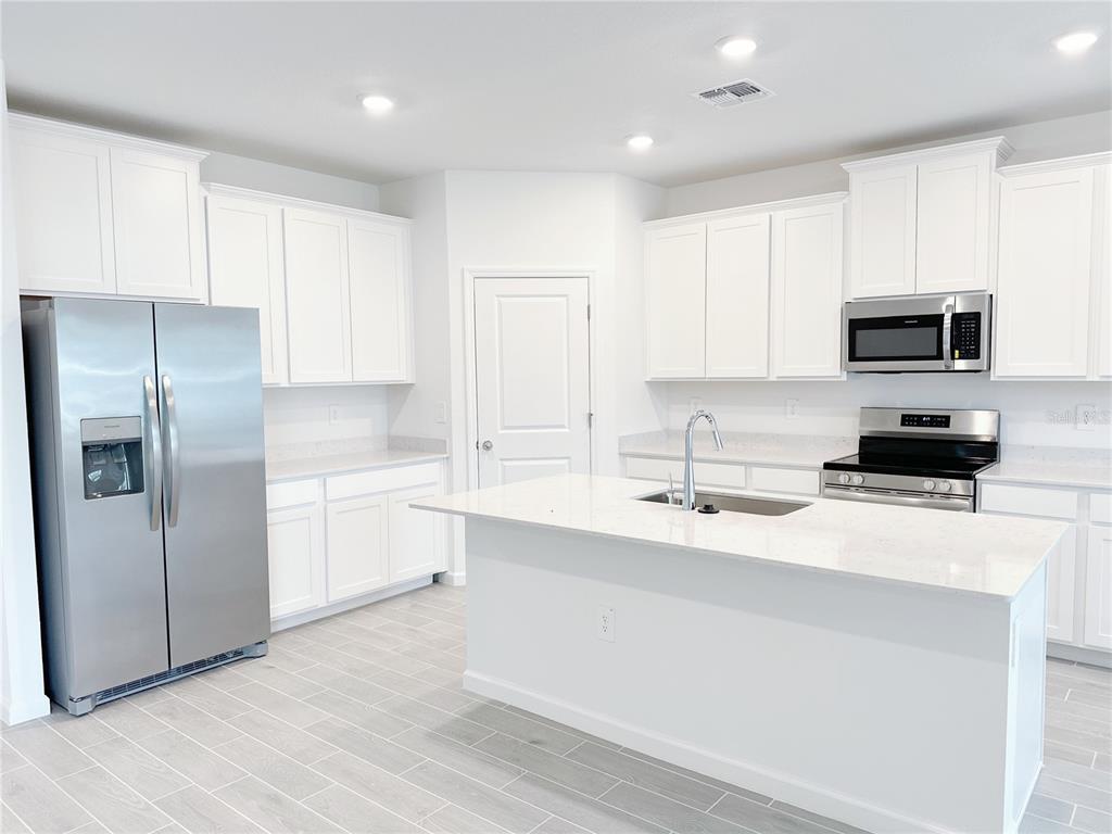 A modern kitchen features white cabinets, stainless steel appliances, a center island, and light flooring — 6583 SW 89TH LOOP, OCALA, FL