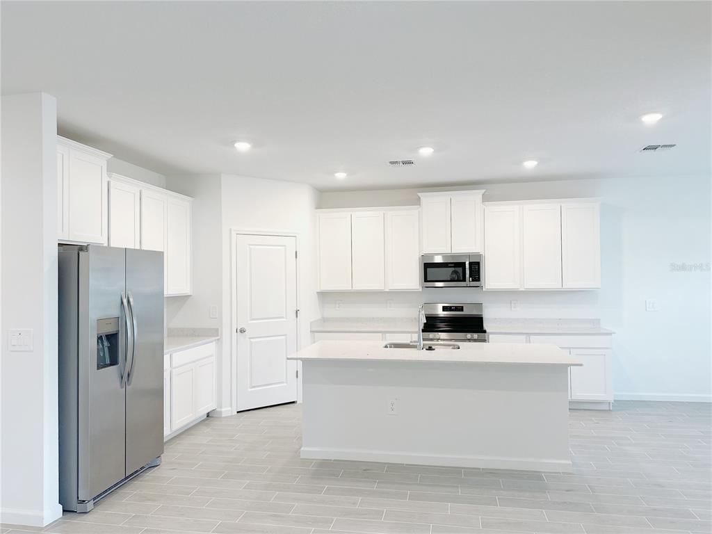 A modern kitchen features white cabinets, stainless steel appliances, a center island, and light flooring — 6583 SW 89TH LOOP, OCALA, FL