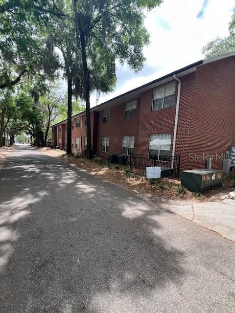 A multi-story brick apartment building stands along a paved road lined with large trees — 120 NW 9TH STREET, GAINESVILLE, FL