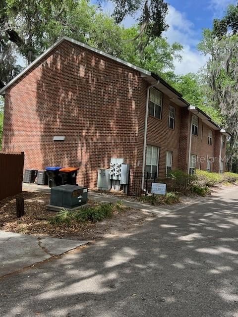 A side view of a two-story brick apartment building with dumpsters and utility equipment outside — 120 NW 9TH STREET, GAINESVILLE, FL