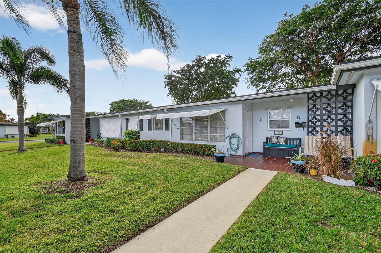 A single-story residential building with a concrete walkway, palm tree, and unit D entrance — 615 High Point Drive # C, Delray Beach FL 33445, DELRAY BEACH, FL