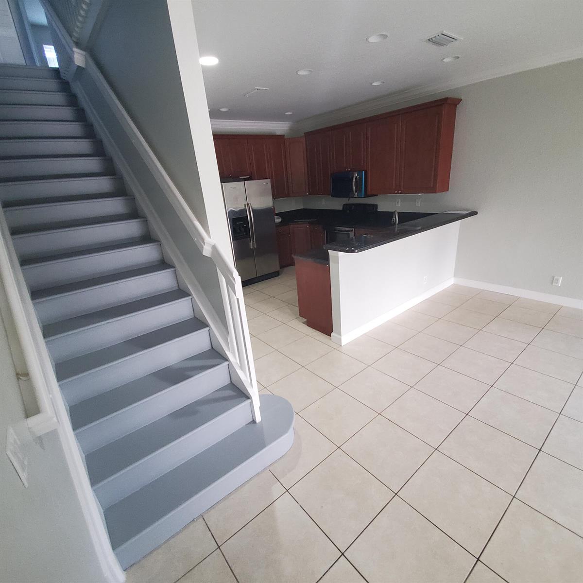 A kitchen with dark wood cabinets and a breakfast bar sits beside a gray staircase — 115 Akron Street # C, FL 33461, FL