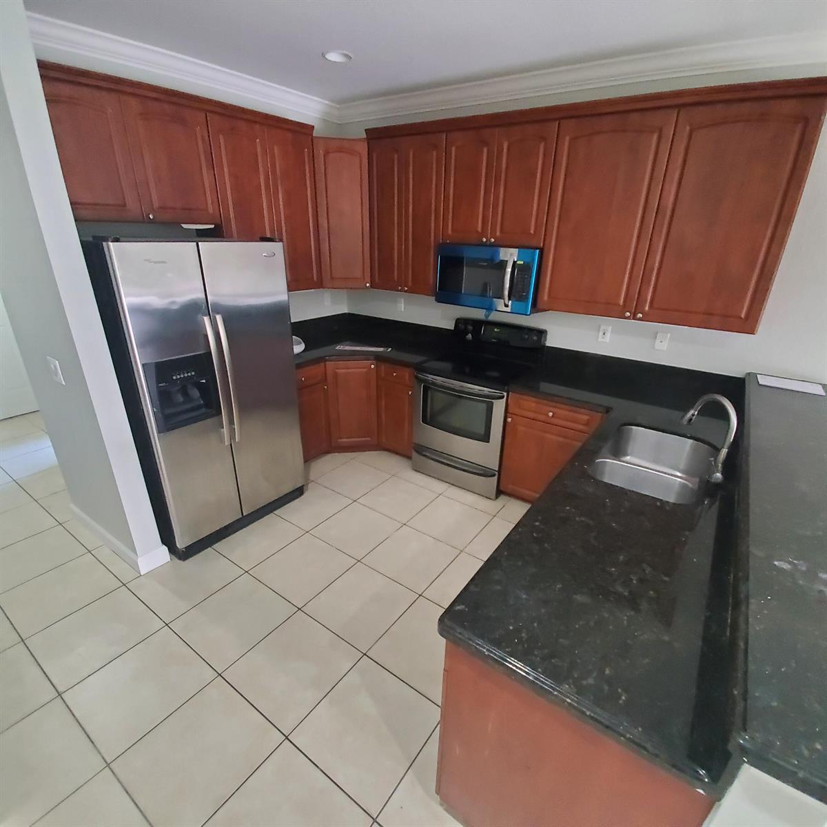 A kitchen features cherry wood cabinets, black granite countertops, stainless steel appliances, and tiled flooring — 115 Akron Street # C, FL 33461, FL