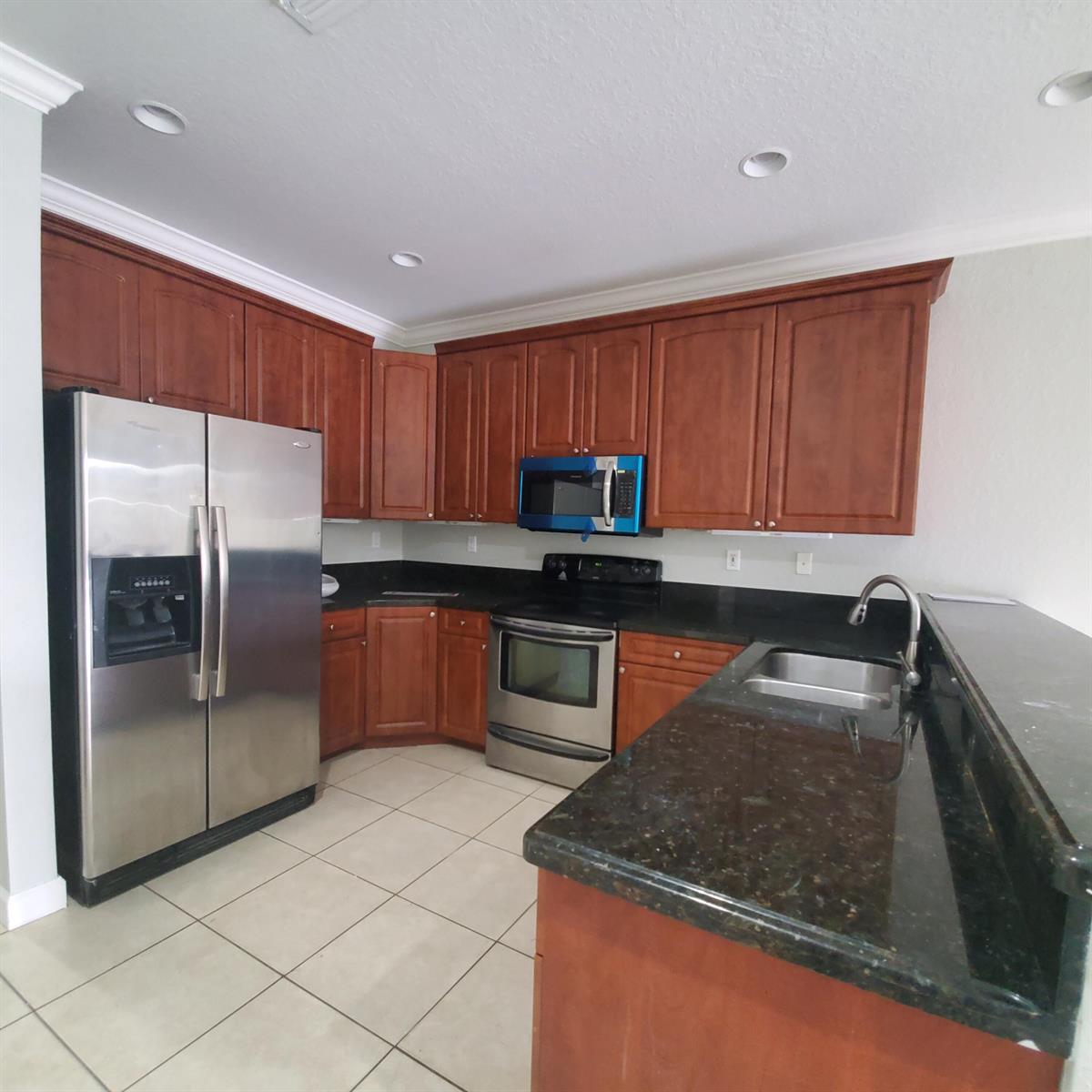 A kitchen features cherry wood cabinets, dark granite countertops, and stainless steel appliances — 115 Akron Street # C, FL 33461, FL