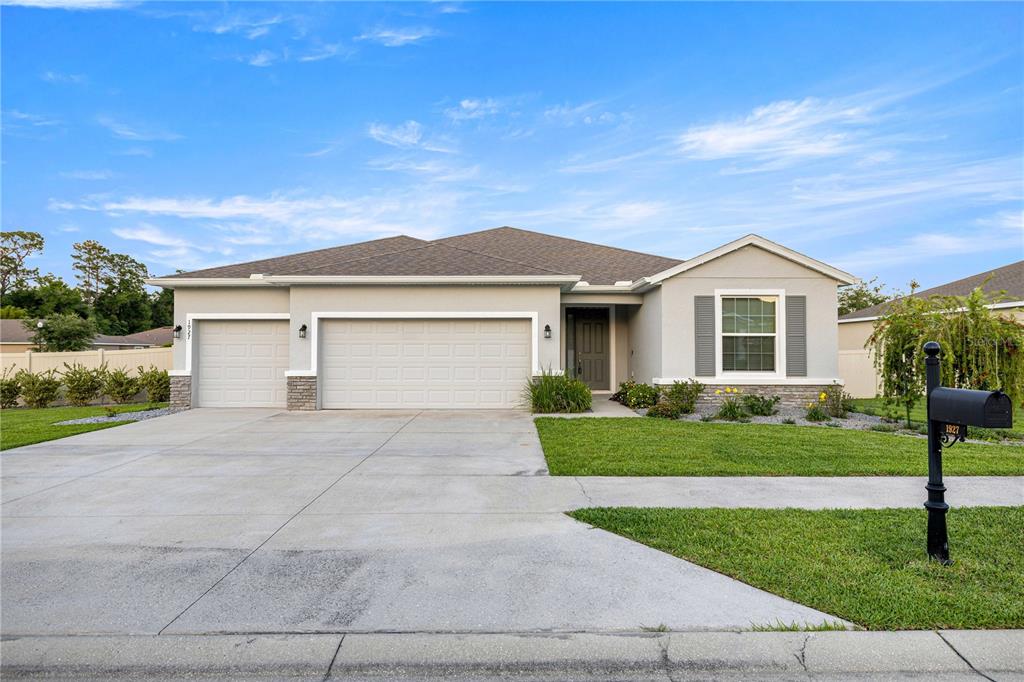 A single-story house with a three-car garage, gray stucco exterior, and a manicured lawn — 1927 NE 50TH COURT, OCALA, FL
