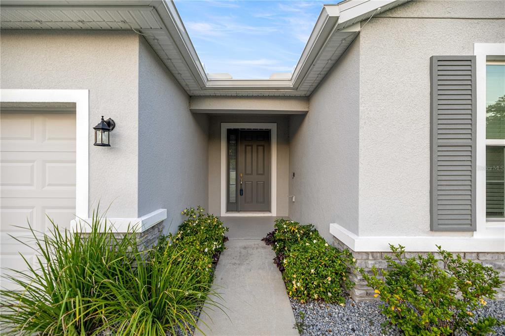 A gray front door is centered between a garage and a window with shutters — 1927 NE 50TH COURT, OCALA, FL