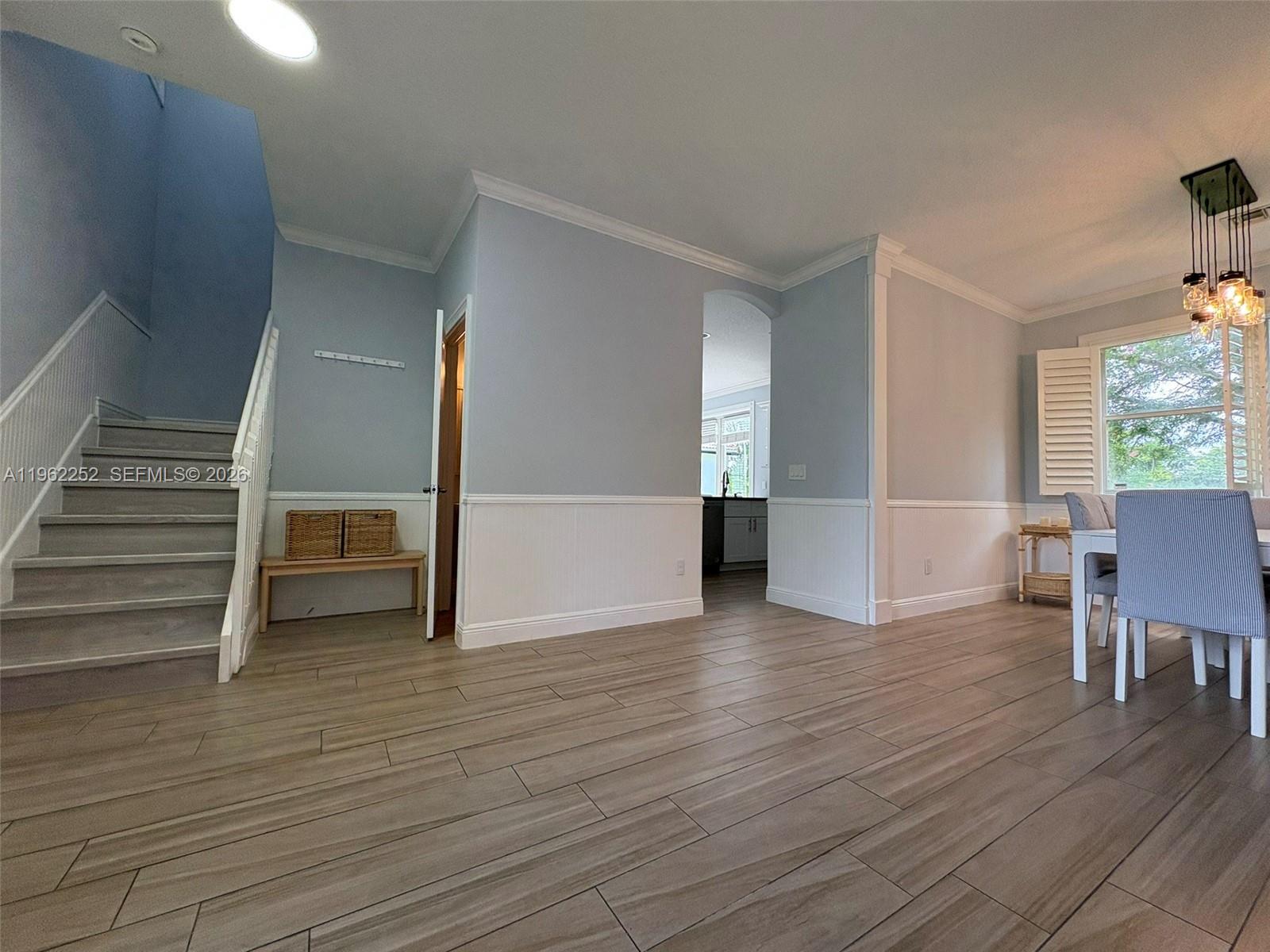 A dining area with wood-look tile flooring, wainscoting, and a staircase leading to an upper level — 10793 Oak Bend Way, Wellington FL 33414, WELLINGTON, FL