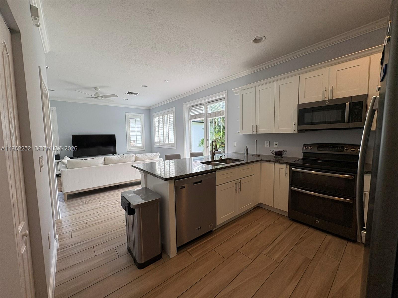 A kitchen with white cabinets, granite countertops, and stainless steel appliances opens to a living area — 10793 Oak Bend Way, Wellington FL 33414, WELLINGTON, FL