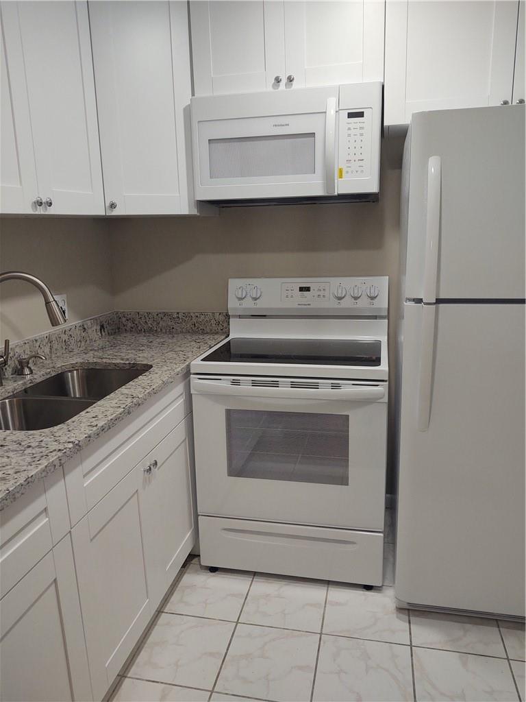 A kitchen features white cabinets, a white stove, a microwave, and a granite countertop — 16 Keswick A # 16, Deerfield Beach FL 33442, DEERFIELD BEACH, FL