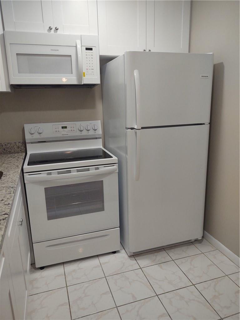 A kitchen features white appliances, white cabinets, granite countertops, and light-colored tile flooring — 16 Keswick A # 16, Deerfield Beach FL 33442, DEERFIELD BEACH, FL