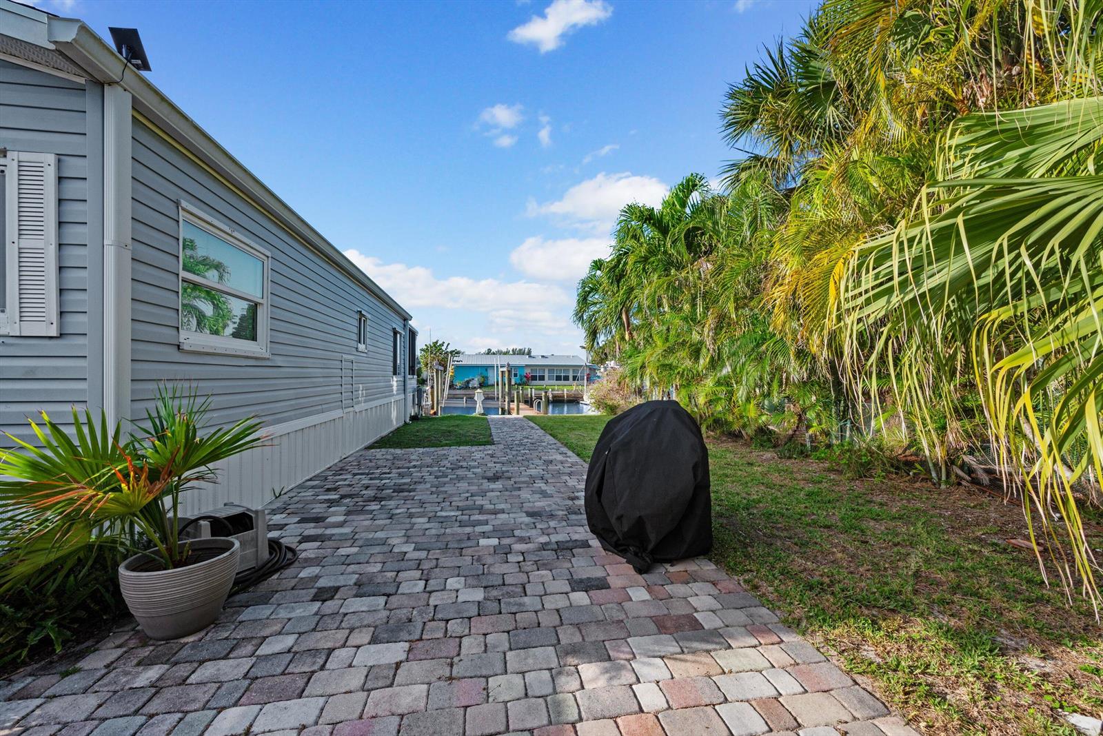 A paved walkway leads past a house and grill cover toward a canal with docks — 10851 S Ocean Drive, Jensen Beach FL 34957, JENSEN BEACH, FL