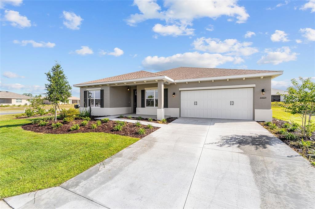 A single-story house with a beige stucco exterior, a two-car garage, and a concrete driveway — 10665 SW 101ST LANE ROAD, OCALA, FL