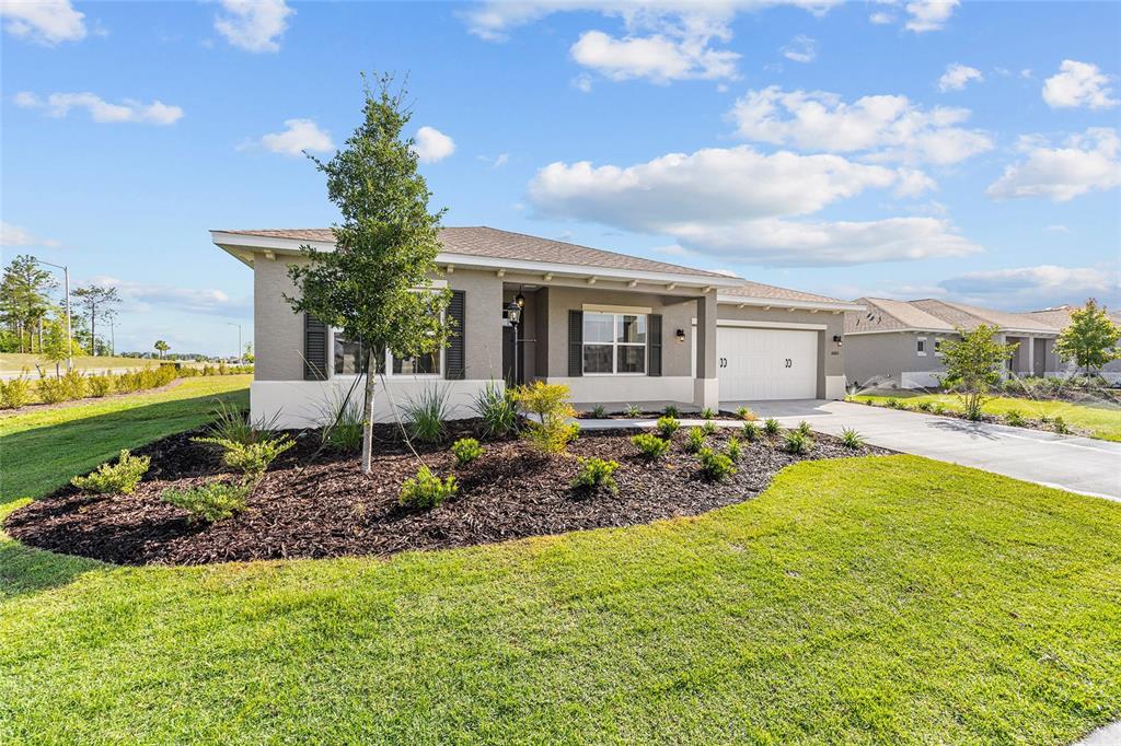 A single-story house with a tan exterior, a two-car garage, and a landscaped front yard — 10665 SW 101ST LANE ROAD, OCALA, FL