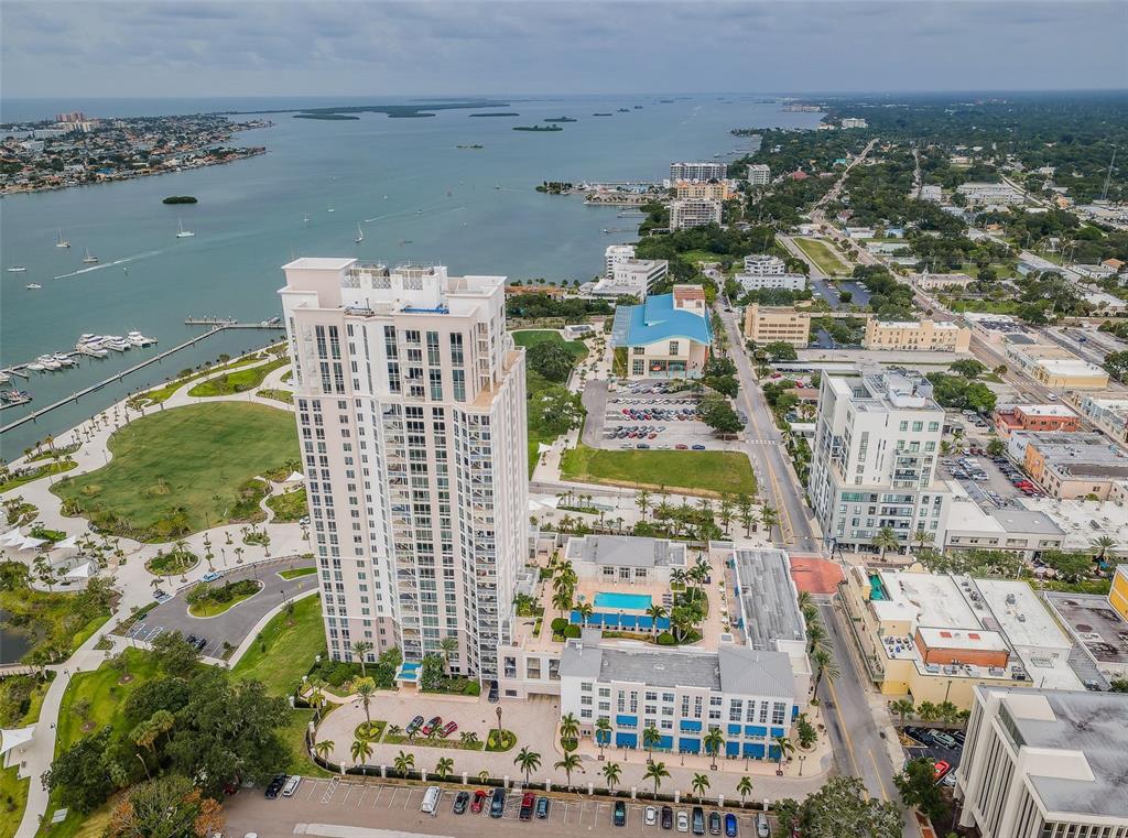 An aerial view shows a tall residential tower beside a waterfront park and marina — 331 CLEVELAND STREET UNIT 310, CLEARWATER, FL