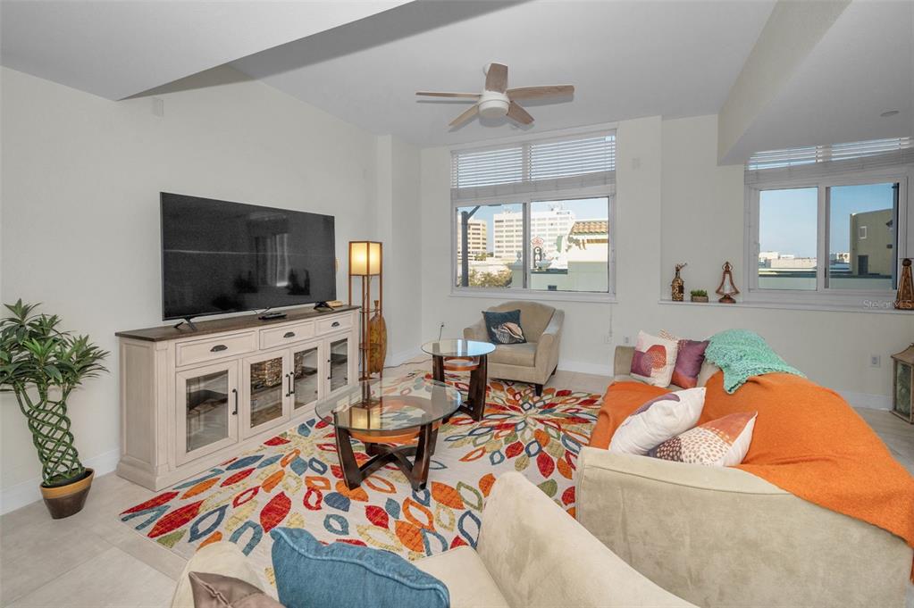 A living room features a colorful patterned rug, a large television, and two windows — 331 CLEVELAND STREET UNIT 310, CLEARWATER, FL