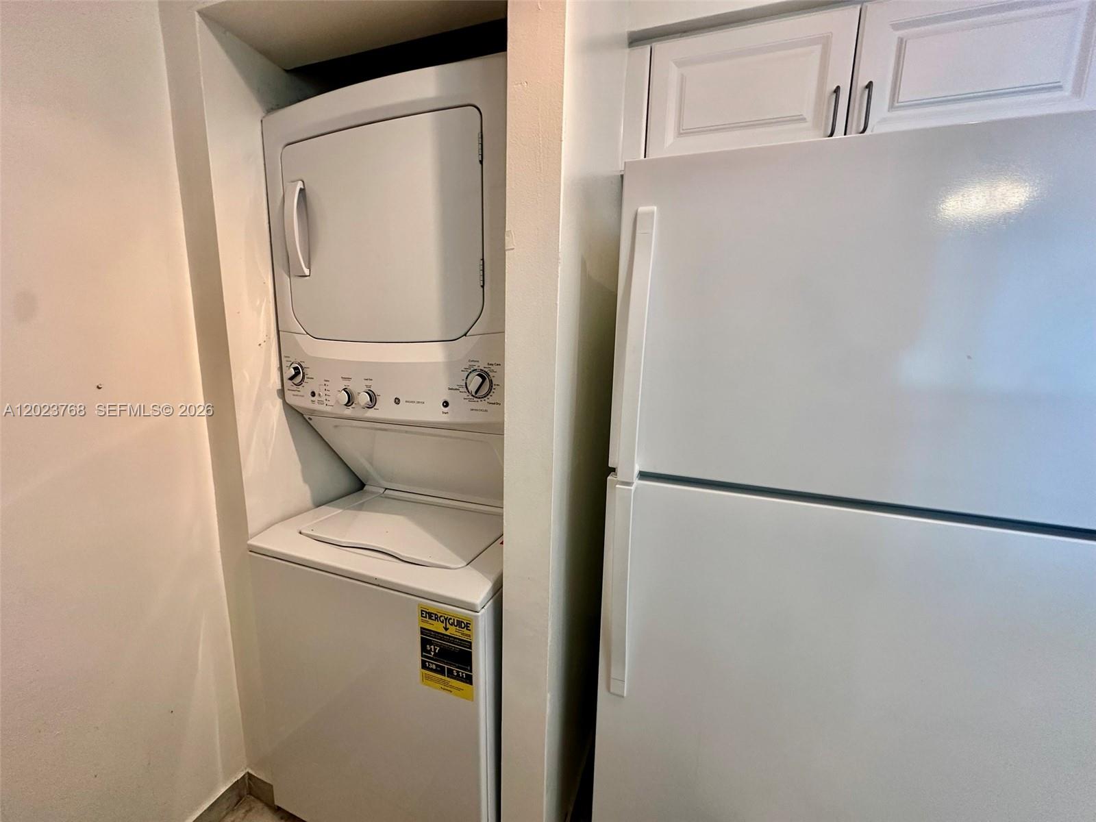 A white stacked washer and dryer unit sits next to a white refrigerator — 1155 Brickell Bay Dr # 905, Miami FL 33131, MIAMI, FL