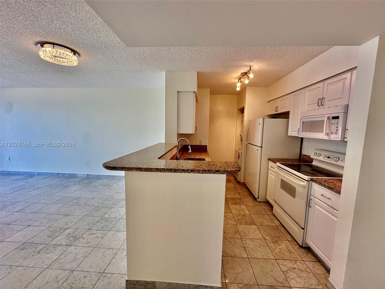 A kitchen with white cabinets, granite countertops, and white appliances opens to a tiled room — 1155 Brickell Bay Dr # 905, Miami FL 33131, MIAMI, FL