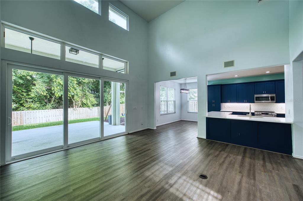 A living room with high ceilings, wood-look flooring, sliding glass doors, and an open kitchen — 228 36TH STREET NE, BRADENTON, FL