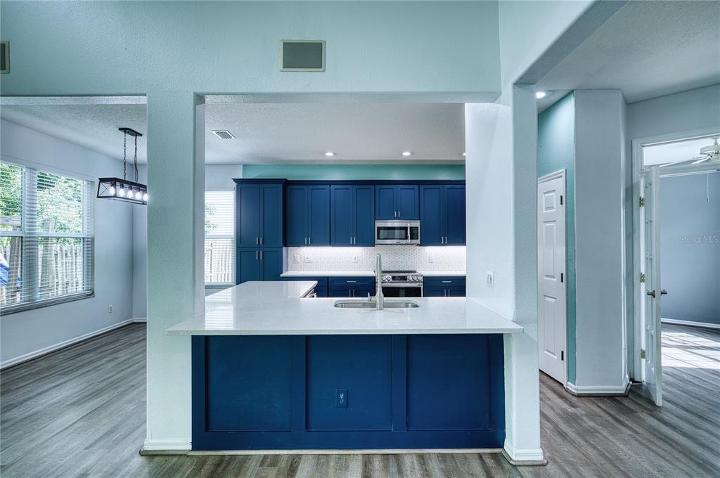 A kitchen features blue cabinets, white countertops, and a breakfast bar overlooking a dining area — 228 36TH STREET NE, BRADENTON, FL