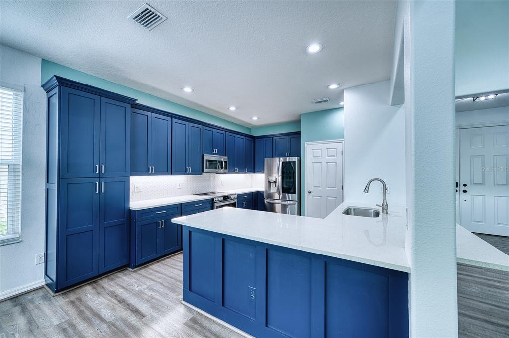 A kitchen features blue cabinets, white countertops, stainless steel appliances, and light wood-look flooring — 228 36TH STREET NE, BRADENTON, FL