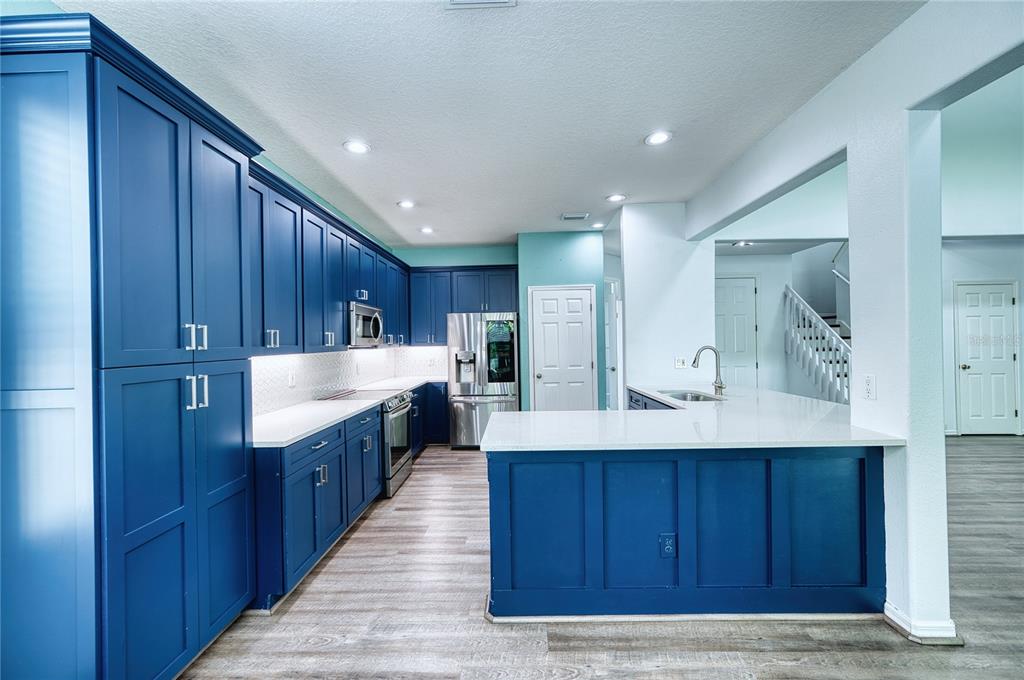 A kitchen features blue cabinetry, white countertops, stainless steel appliances, and light wood-look flooring — 228 36TH STREET NE, BRADENTON, FL