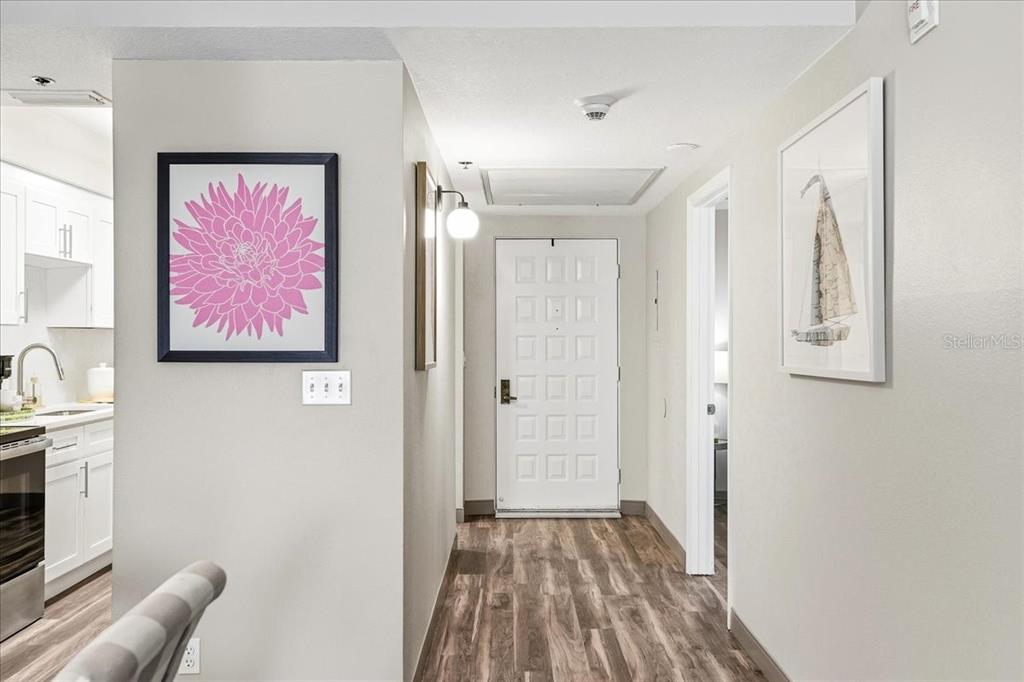 A hallway with wood-look flooring leads to a white front door with glass panels — 4540 BEE RIDGE ROAD UNIT 175, SARASOTA, FL