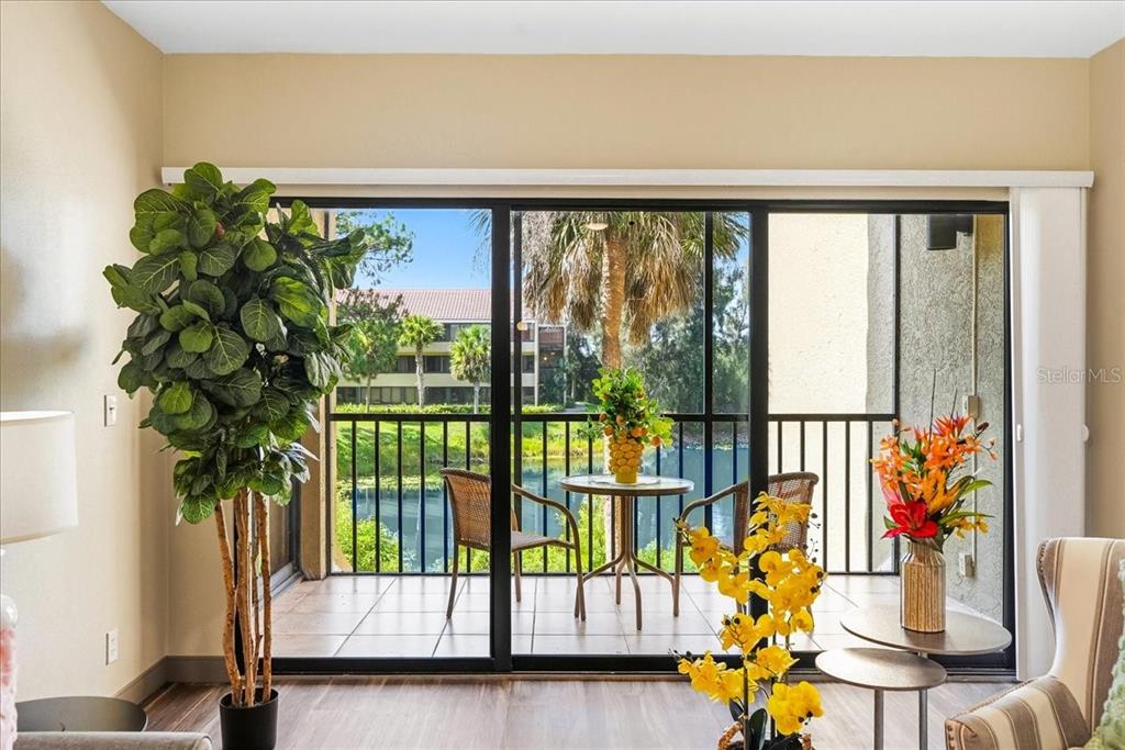A living room looks out through sliding glass doors onto a screened balcony overlooking water — 4540 BEE RIDGE ROAD UNIT 175, SARASOTA, FL