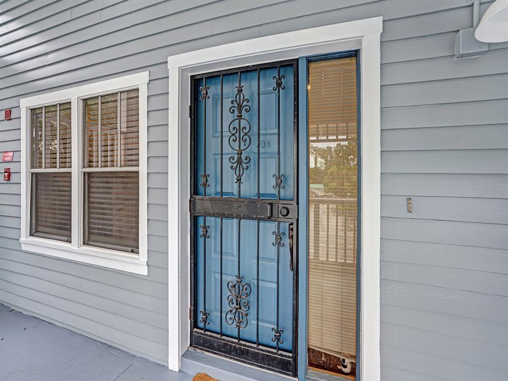 A blue front door with a decorative security gate and an adjacent window on gray siding — 2511 DOLLY BAY DRIVE UNIT 308, PALM HARBOR, FL