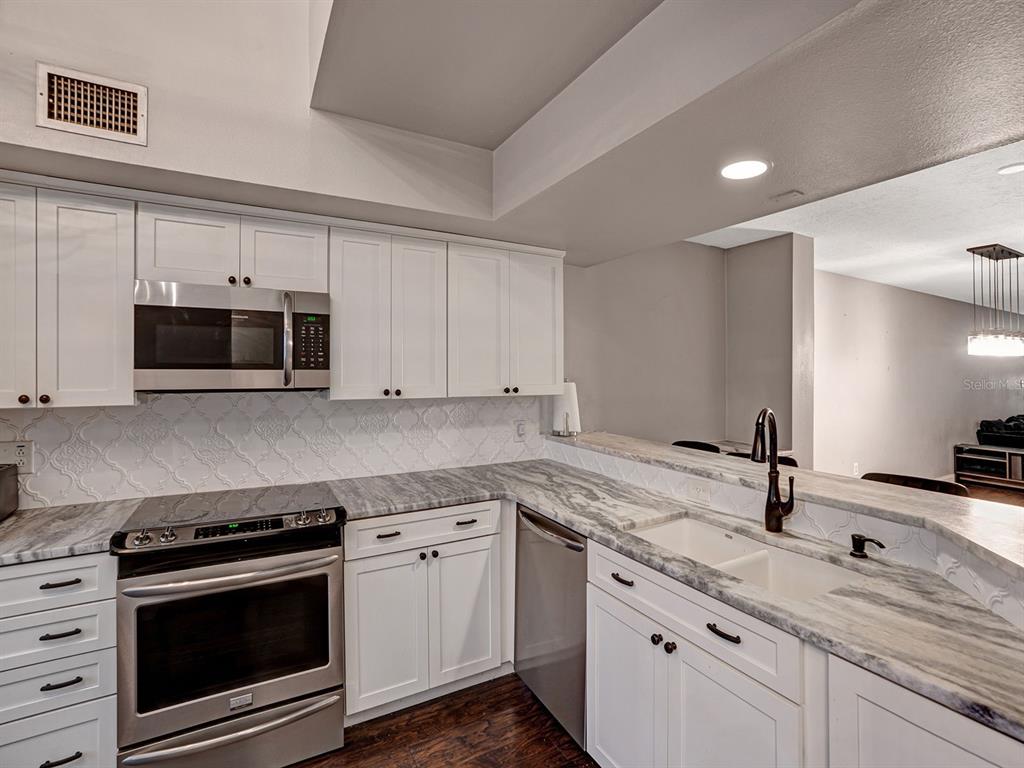 A kitchen features white cabinets, stainless steel appliances, and gray-veined stone countertops — 2511 DOLLY BAY DRIVE UNIT 308, PALM HARBOR, FL