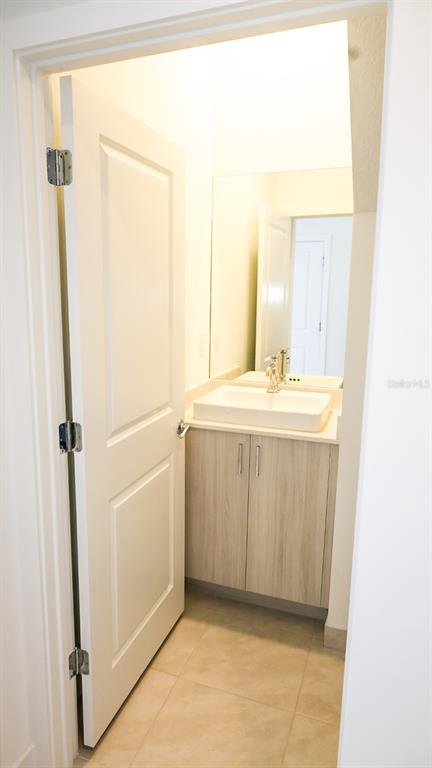 A small bathroom features a light wood vanity, a white vessel sink, and tile flooring — 5868 AGOSTINO WAY, IMMOKALEE, FL
