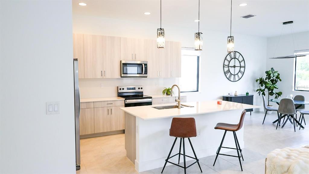 A modern kitchen features light wood cabinets, a white island, and stainless steel appliances — 5868 AGOSTINO WAY, IMMOKALEE, FL