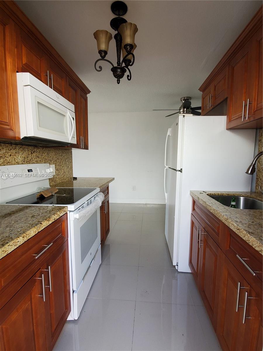 A galley kitchen features wood cabinets, granite countertops, white appliances, and light tile flooring — 808 N 24th Ave # 1, Hollywood FL 33020, HOLLYWOOD, FL