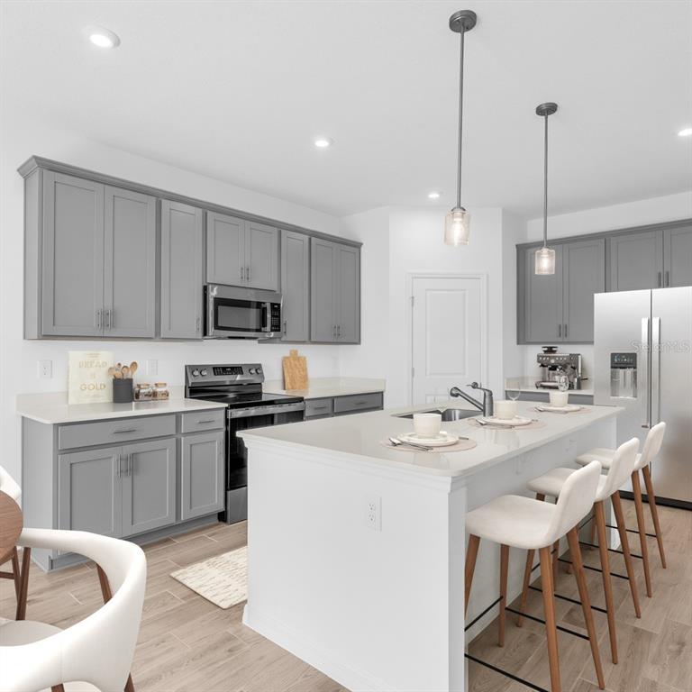 A kitchen features gray cabinets, white countertops, a central island with stools, and stainless appliances — 9210 HARRIS HAWK DRIVE, LEESBURG, FL