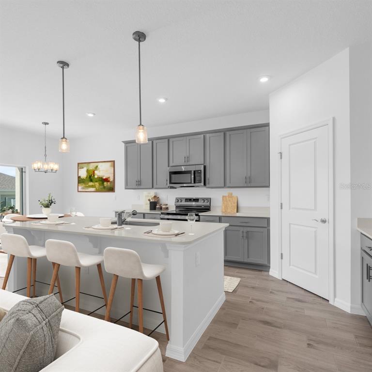 A kitchen features gray cabinets, a white island with bar stools, and light wood flooring — 9210 HARRIS HAWK DRIVE, LEESBURG, FL