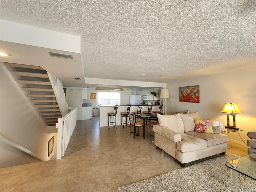 A living room with tile floors, a staircase, and an open kitchen with bar seating — 1101 PINELLAS BAYWAY S UNIT 303, TIERRA VERDE, FL