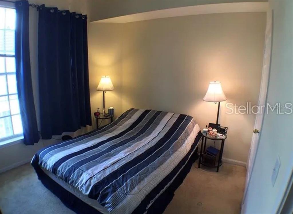 A bedroom features a bed with a striped comforter, two side tables, and blue curtains — 280 CELEBRATION BOULEVARD UNIT 307, CELEBRATION, FL