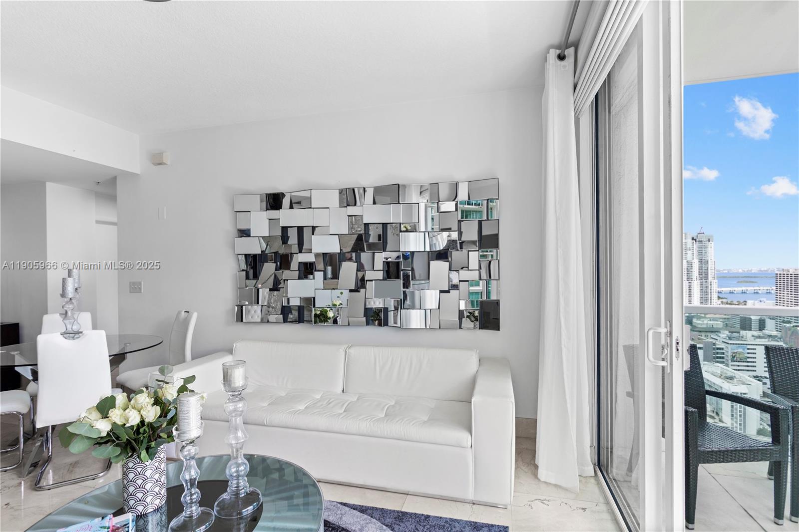 A white sofa sits below a large mosaic mirror in a living room with balcony access — 31 SE 5th St # 4018, Miami FL 33131, MIAMI, FL
