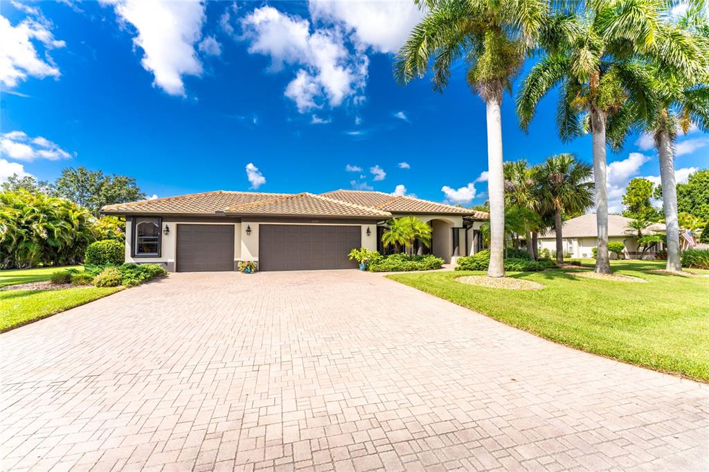 A single-story house with a paved driveway, two garage doors, and tall palm trees — 25279 PUNTA MADRYN AVENUE, PUNTA GORDA, FL