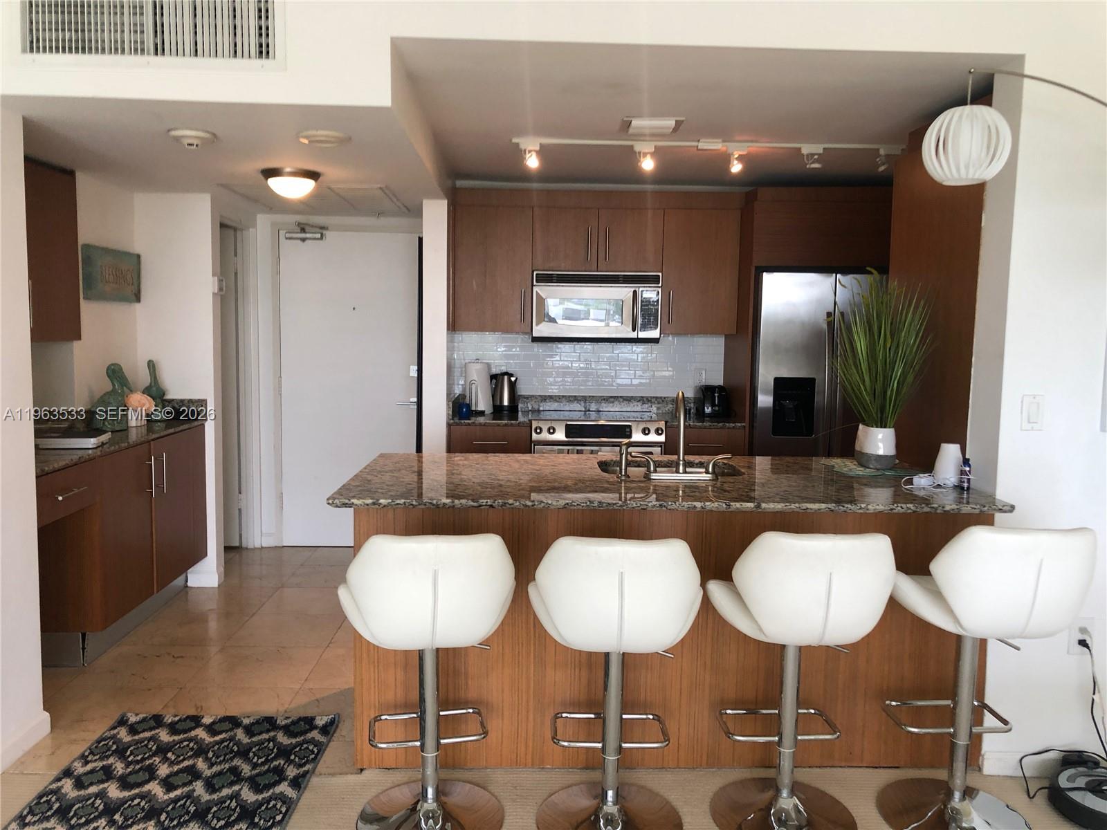 A kitchen features wood cabinets, granite countertops, a breakfast bar with four stools, and appliances — 10275 Collins Ave # 427, Bal Harbour FL 33154, BAL HARBOUR, FL