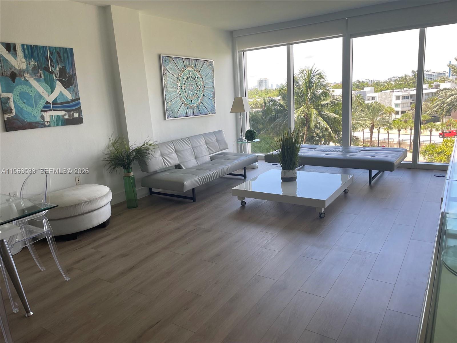 A modern living room features light wood floors, two grey sofas, and floor-to-ceiling windows — 10275 Collins Ave # 427, Bal Harbour FL 33154, BAL HARBOUR, FL