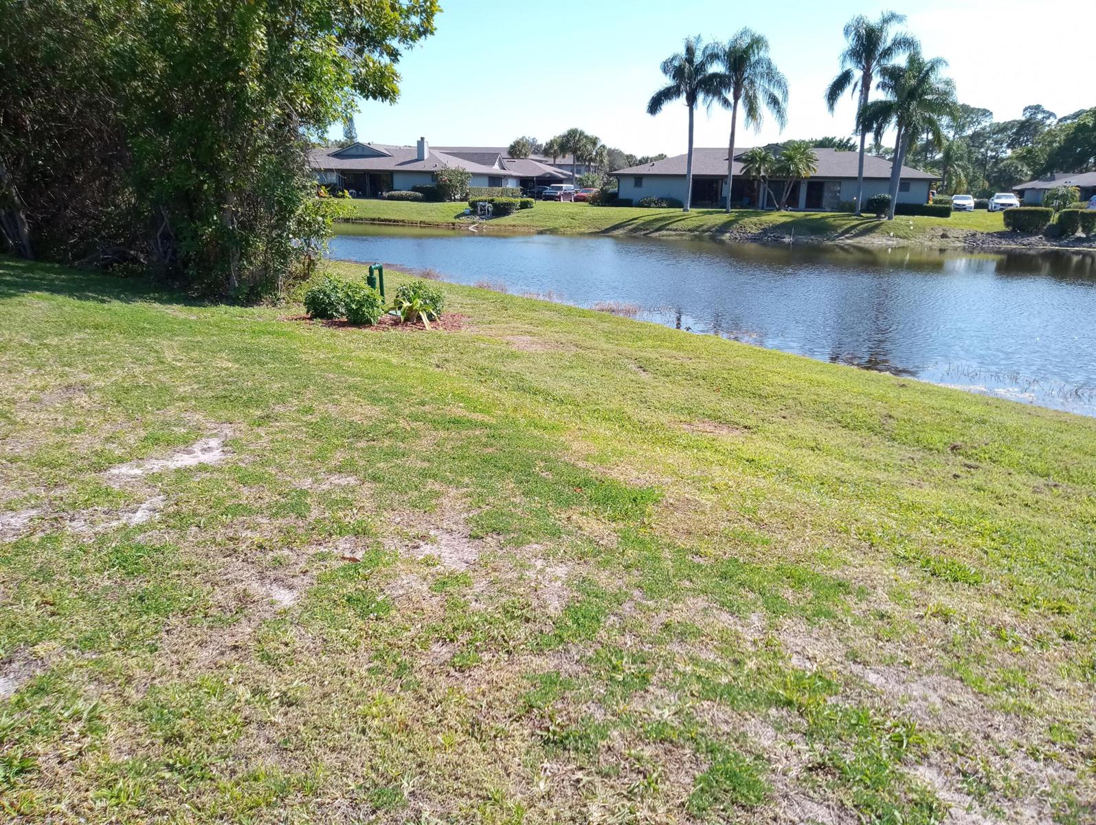 A grassy lawn slopes down toward a pond with residential buildings in the background — 630 E Pointe Ct SW, Vero Beach FL 32962, VERO BEACH, FL